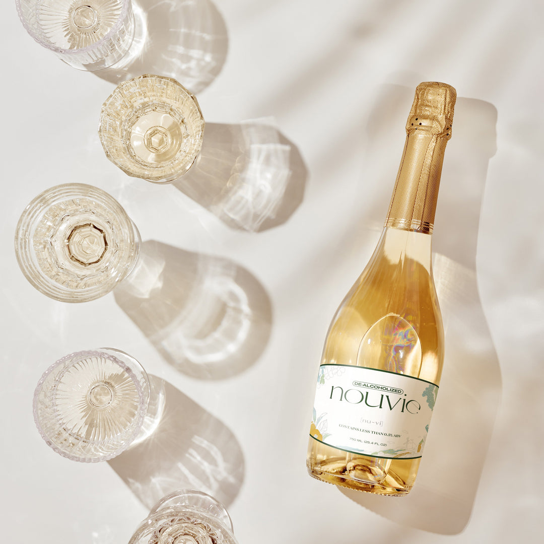 Flat lay of a Nouvie Spanish Sparkling Wine bottle resting on a table, showcasing its elegant label and sleek design, with natural light highlighting the curves of the glass.