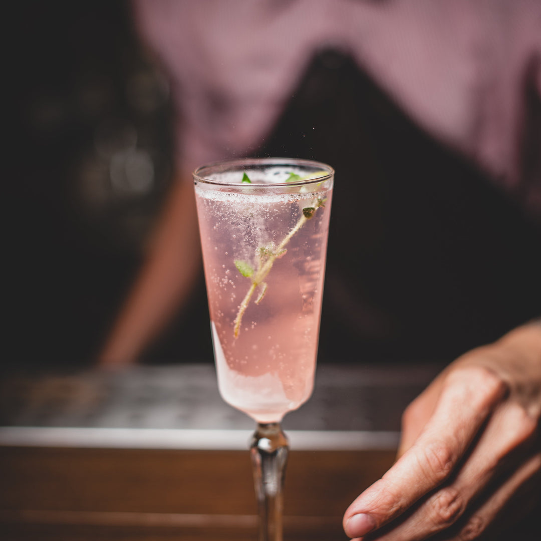 Glass of Nouvie Sparkling White Wine Spritzer on a bar counter, with bubbles rising and a garnish on top, set against a stylish bar backdrop.